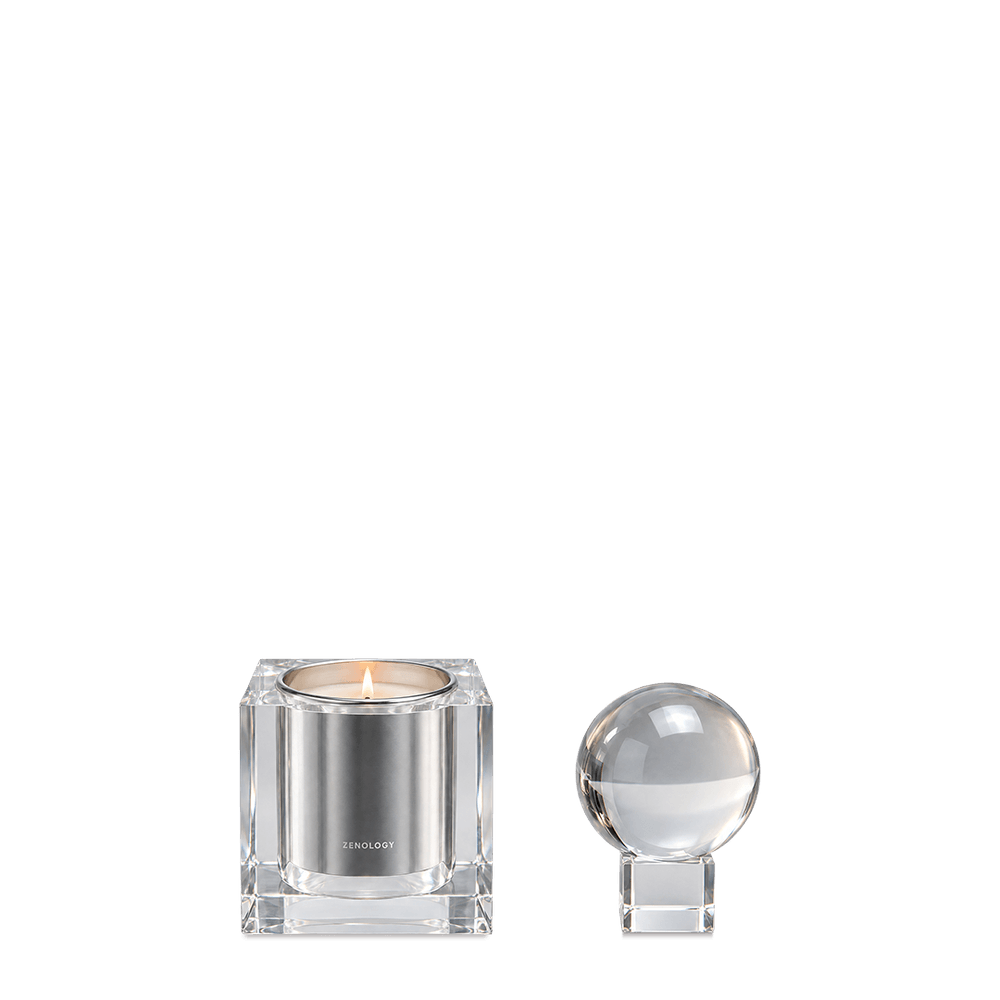 Crystal candle holder with a lit candle and crystal sphere beside it, against a neutral background.